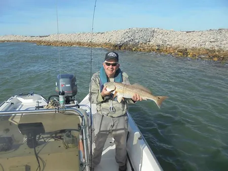 An angler holding a redfish on a boat beside the rock jetty