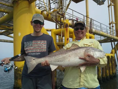Two anglers holding large redfish in front of a yellow offshore platform