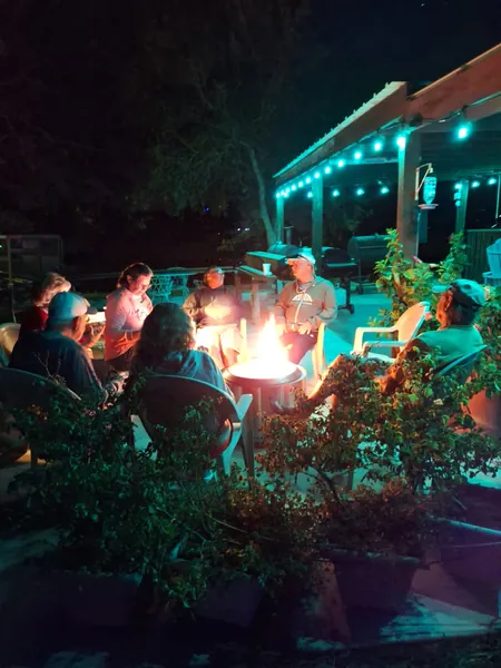 Guests sitting in a circle around a fire pit at night, under strings of teal lights on the pavilion