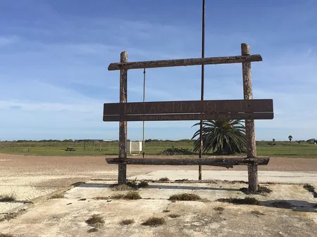 The weathered Matagorda Island and National Wildlife Refuge sign with palms behind it