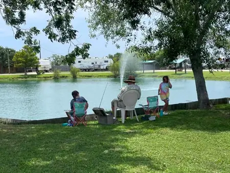 Guests fishing from lawn chairs on the bank of the stocked pond, with the fountain running and RV sites across the water